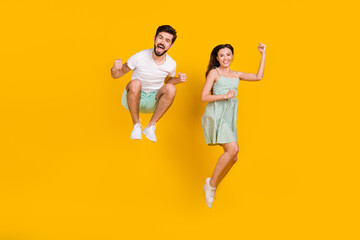 Photo of crazy married couple raise fists jump achieve goal wear casual outfit isolated yellow...
