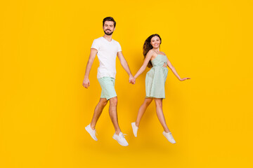 Fototapeta na wymiar Photo of cheerful carefree couple jump hold hands move go wear casual outfit isolated yellow color background