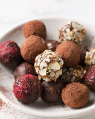 Chocolate candies. Delicious dessert on a light background. Truffles with waffle crumbs, with cocoa. Sweets on a white plate. Macro photography of sweets.