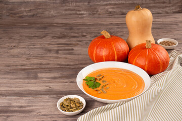 Pumpkin cream soup in white bowl toped with parsley and pumpkin seeds on wooden table background with copy space for text. Vegan food concept, homemade soup recipe. Selective focus