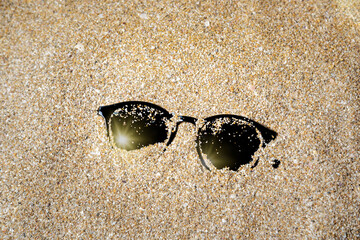 Sunglasses are buried in the sand on the beach.