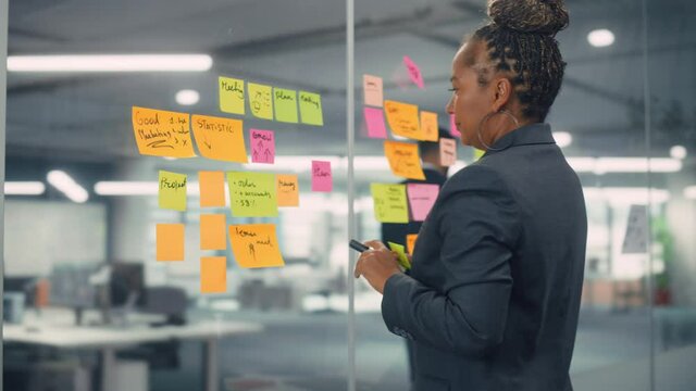 African American Businesswoman Creating Project Plan on Office Wall with Paper Notes. Stylish Confident Manager Working on Business, Financial and Marketing Projects. Specialist in Diverse Team.
