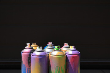 Used cans of spray paint near black wall, space for text. Graffiti supplies