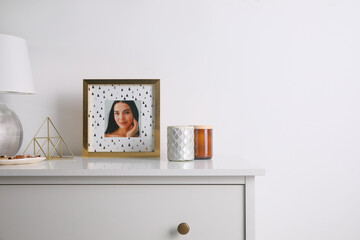 Photo frame with portrait of beautiful young woman near stylish decor on white commode. Space for text