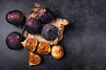 Fresh and dried figs on a dark background. Several ripe figs, one cut and dried figs lie on a dark concrete background and craft paper packaging. Still life with healthy fruits