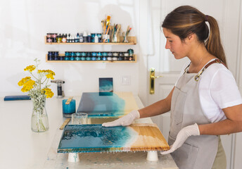 Young Female artist spreading resin over an artistic picture of the sea