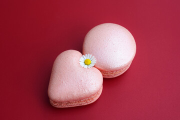 Delicious pink heart and round shape macarons, decorated with edible daisy flower, red background