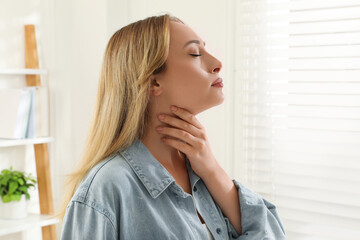Young woman doing thyroid self examination near window at home