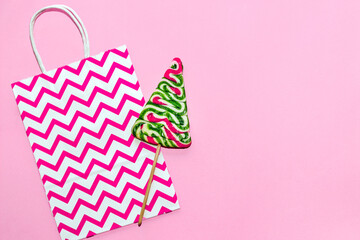 Christmas tree shaped lollipop with gift bag on pink background.