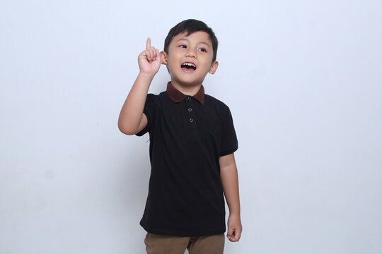 The Asian boy who was wearing a black t-shirt looked to the side with his index finger raised with an expression as if he had an idea. White background. 