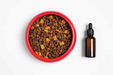 Glass bottle of tincture near dry pet food in bowl on white background, top view
