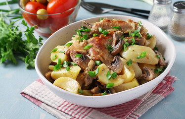 Rabbit meat with potatoes and mushrooms in a light plate on a light blue background. Close-up