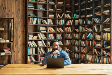 Smart intelligent Indian male freelancer in casual wear using laptop in modern office with...