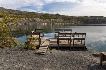 Pontoon with a wooden table and benches for relaxation is on the blue water of the lake