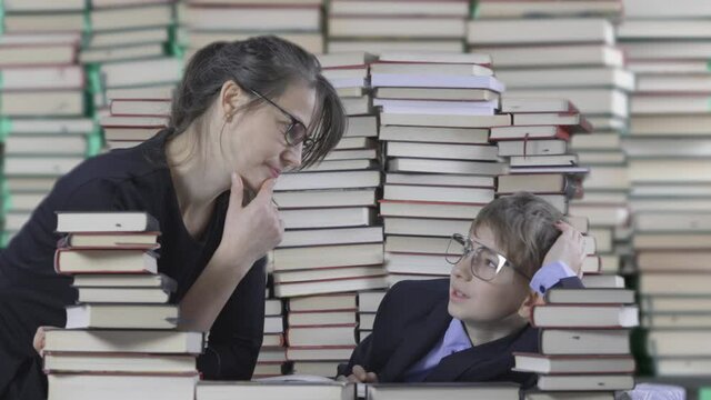 Mother with eyeglasses teach boy in suit in a library, naughty child