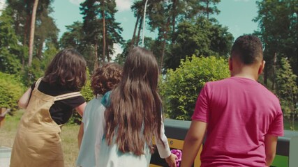 Group of adorable multiethnic diverse children throwing plastic garbage and glass bottle in metal recycle trash container in public park. Young people sorting waste, helping environment