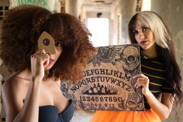 two young and beautiful women, one blonde and one African-American, doing the Ouija board in a...