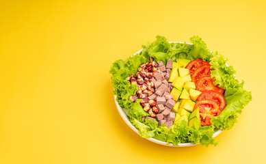 Green lettuce salad with fresh mixed purple corn, purple yams, avocado, and tomatoes on a yellow background. Space for text. Concept of healthy foods and vegetables