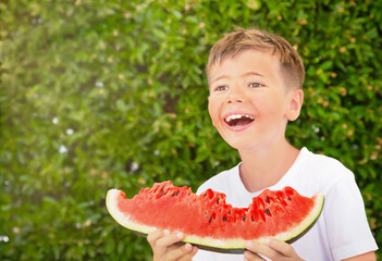 Happy child (boy) is eating a red juicy watermelon. Caucasian kid smiling .and having fun. Concept of healthy food, happy childhood, summer vacation. Nature background. Copy space.