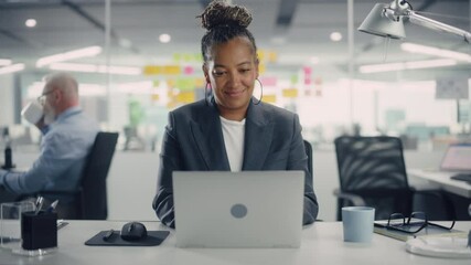 Portrait of a Happy African American Businesswoman Using Laptop Computer in Modern Office. Stylish Beautiful Manager Smiling, Working on Financial and Marketing Projects. Camera Zoom In. - Powered by Adobe