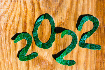 the numbers of the new year 2022 are cut from green leaves and are on a wooden background