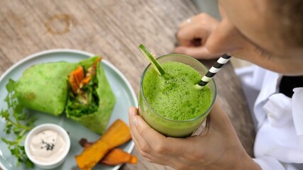 Top shot of woman takes a sip of her green vegetable detox juice through the paper straw.Vegan kebab on the table