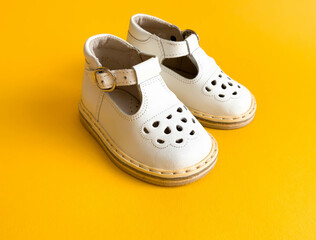 Children's shoes, the concept of the first step. Baby white on a yellow colorful background. Space for the text. The first steps of the baby. Children's background. Orthopedics. Top view, layout