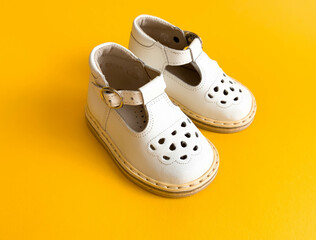 Children's shoes, the concept of the first step. Baby white on a yellow colorful background. Space for the text. The first steps of the baby. Children's background. Orthopedics. Top view, layout