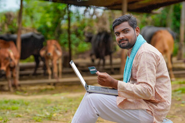 Obraz premium Young indian farmer using laptop and card at his farm