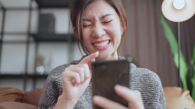 social media enjoy,asian female adult smile laugh hand seach surf smartphone device social media addict at sofa living room home interior background,home quarantine concept