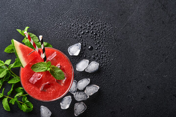Glass of watermelon Margarita cocktail with mint and ice. Summer refreshing drinks in glasses on black table. Concept of healthy summer eating.