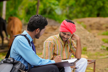 Obraz na płótnie Canvas young india bank officer completing paper work with farmer at his farm.