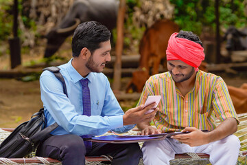 Young indian banker or agronomist showing some detail to farmer in smartphone.
