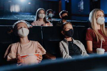 Fototapeta na wymiar Mother with happy small children watching film in the cinema, coronavirus concept.