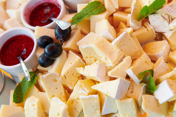 Cheese plate with raspberry jam decorated with mint and blue grape. Brie and goat cheese. Luxury catering. Closeup.