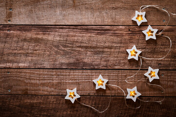 Christmas garland with wooden light stars on old dark wooden background. Top view with copy space. Christmas greeting card.