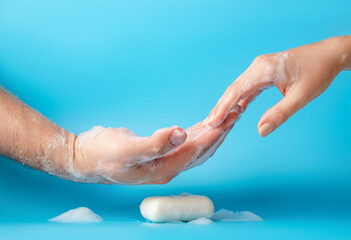 Global Handwashing Day, personal hygiene concept. Male and female hand in soapy blue background.