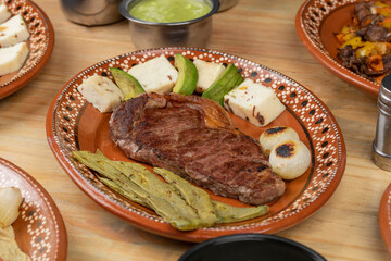 Mexican food, cut of meat served on a plate with nopal, avocado and onion on a wooden table