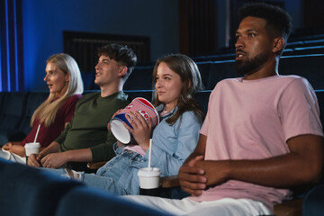 Young people with popcorn adn drinks in the cinema, watching thriller film.
