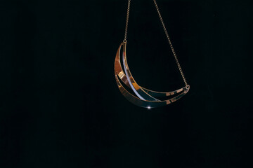 A gold and diamond necklace in the shape of a crescent moon hanging from gold chain, black...