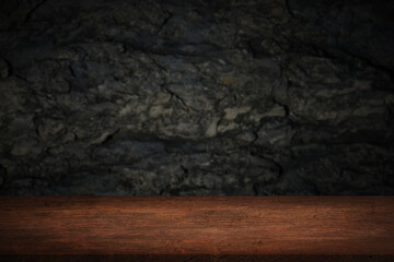 Free space on a wooden table for displaying products with a blurred black wall background.	