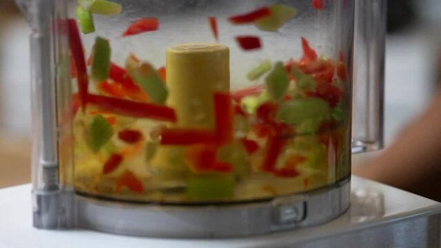 Closeup of green and red bell peppers being chopped in a food processor 