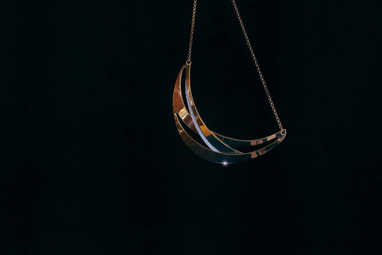 A gold and diamond necklace in the shape of a crescent moon hanging from gold chain, black background, nobody