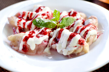 Cherry dumplings sprinkled with strawberry syrup on a white plate. Dumplings with berries for breakfast. A sweet dish popular in Eastern Europe