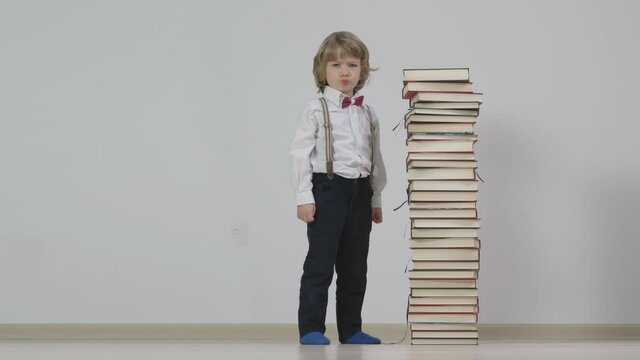 Little serious kid teaching near big tower stack of books
