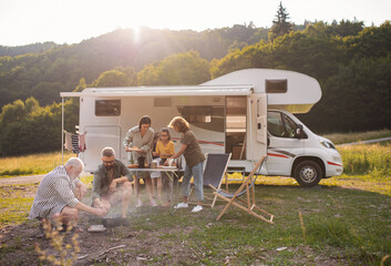 Multi-generation family sitting and eating outdoors by car, caravan holiday trip. - obrazy, fototapety, plakaty