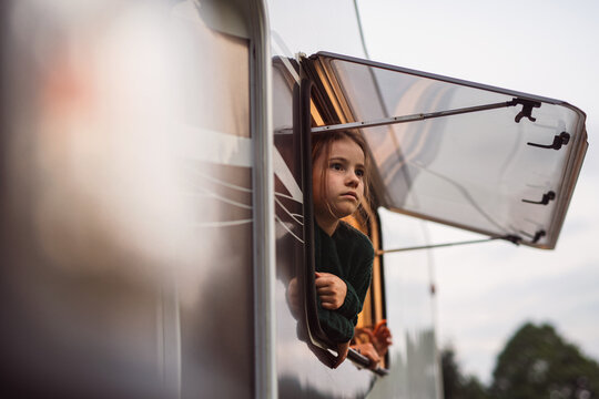 Small girl looking out through caravan window, family holiday trip.