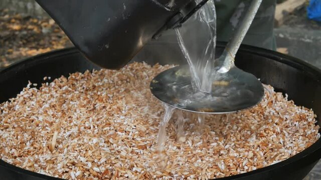 The cook pours hot water into the pilaf through a Skimmer, this is the cooking technology. man prepares Uzbek pilaf in a cauldron in the open air. Close up, slow motion.