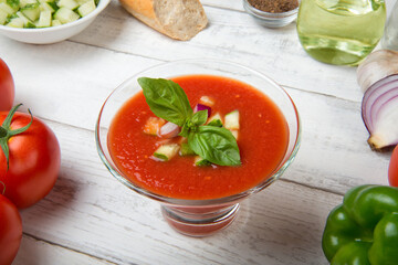 Gazpacho. Traditional Spanish tomato soup with fresh tomatoes, cucumber, bell pepper and basil on a white rustic wooden table.