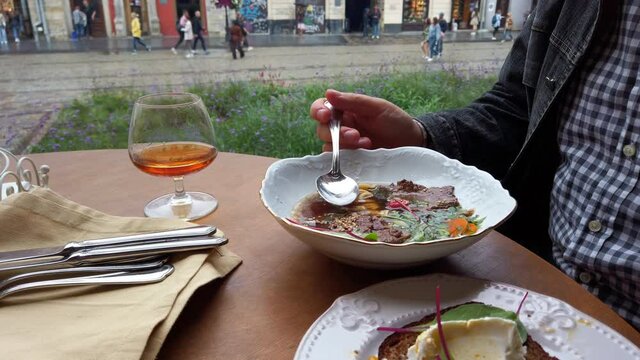 A man eats soup in a restaurant and drinks cognac.